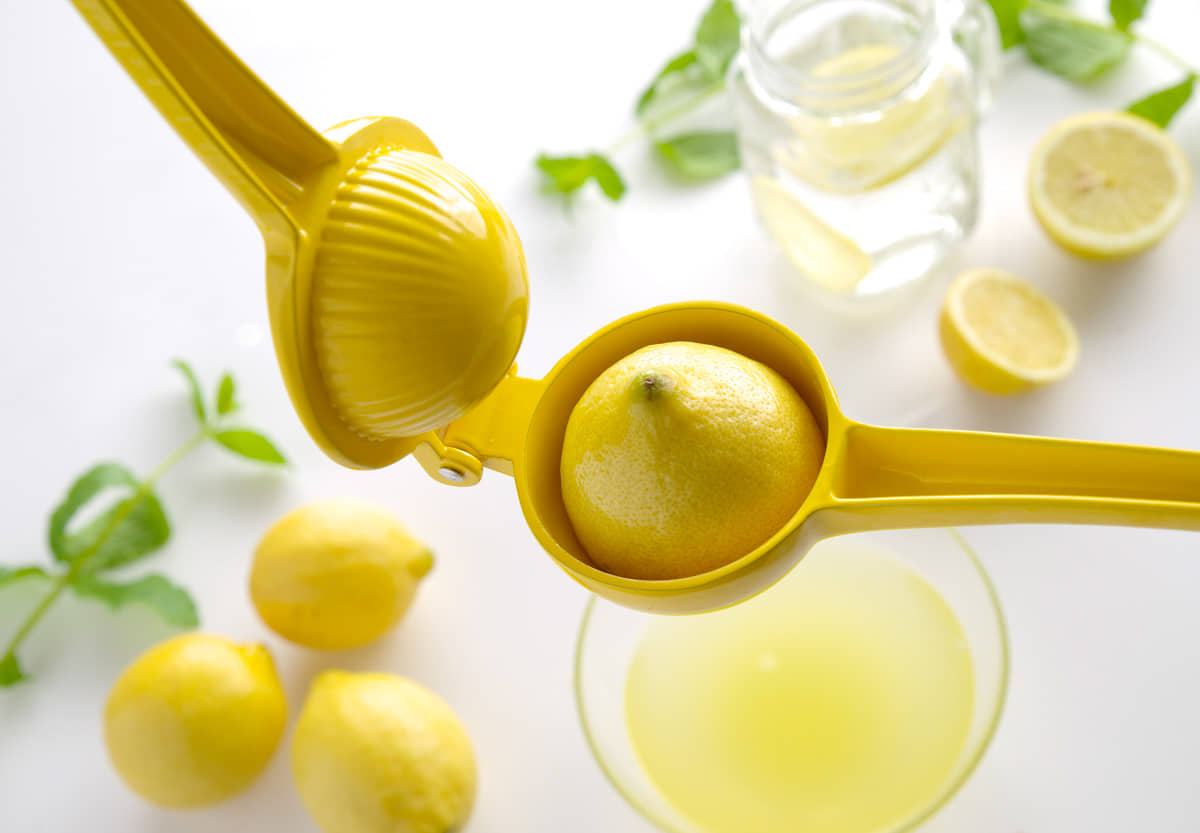 Zitronen mit gelber Handsaftpresse ausdrücken