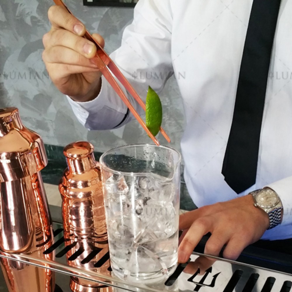 Pinzetten für Cocktailzutaten und Küche Limettenstück wird mit kupferner Pinzette in ein Cocktail Rührglas gelegt
