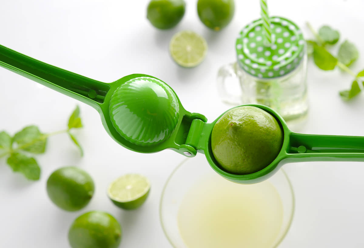 Limetten mit grüner Handsaftpresse ausdrücken