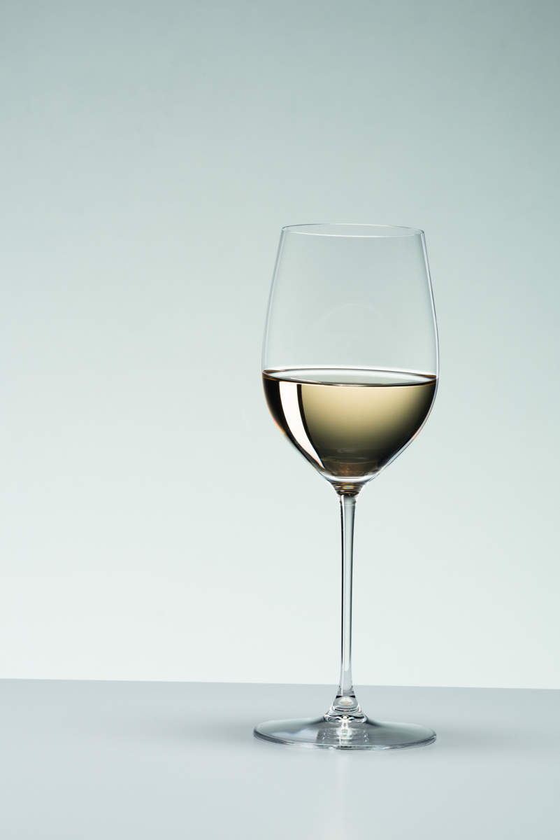 Mit Wein gefülltes Riedel Glas Veritas Weißweinglas Chardonnay Viognier vor grauem Hintergrund