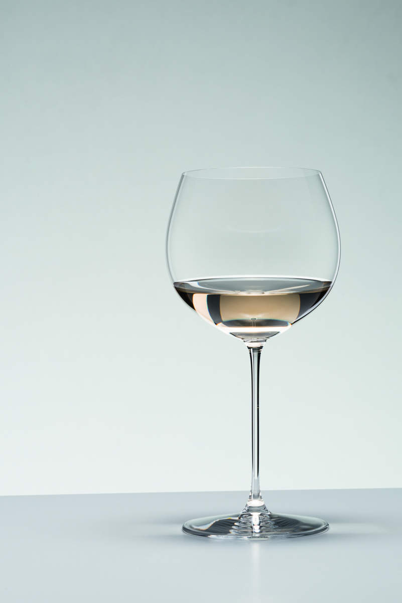 Riedel Glas Veritas Chardonnay Eichenfass Weinglas gefüllt grau Mit Weißwein gefülltes Veritas Weinglas Chardonnay im Fass gereift von Riedel Glas vor grauem Hintergrund